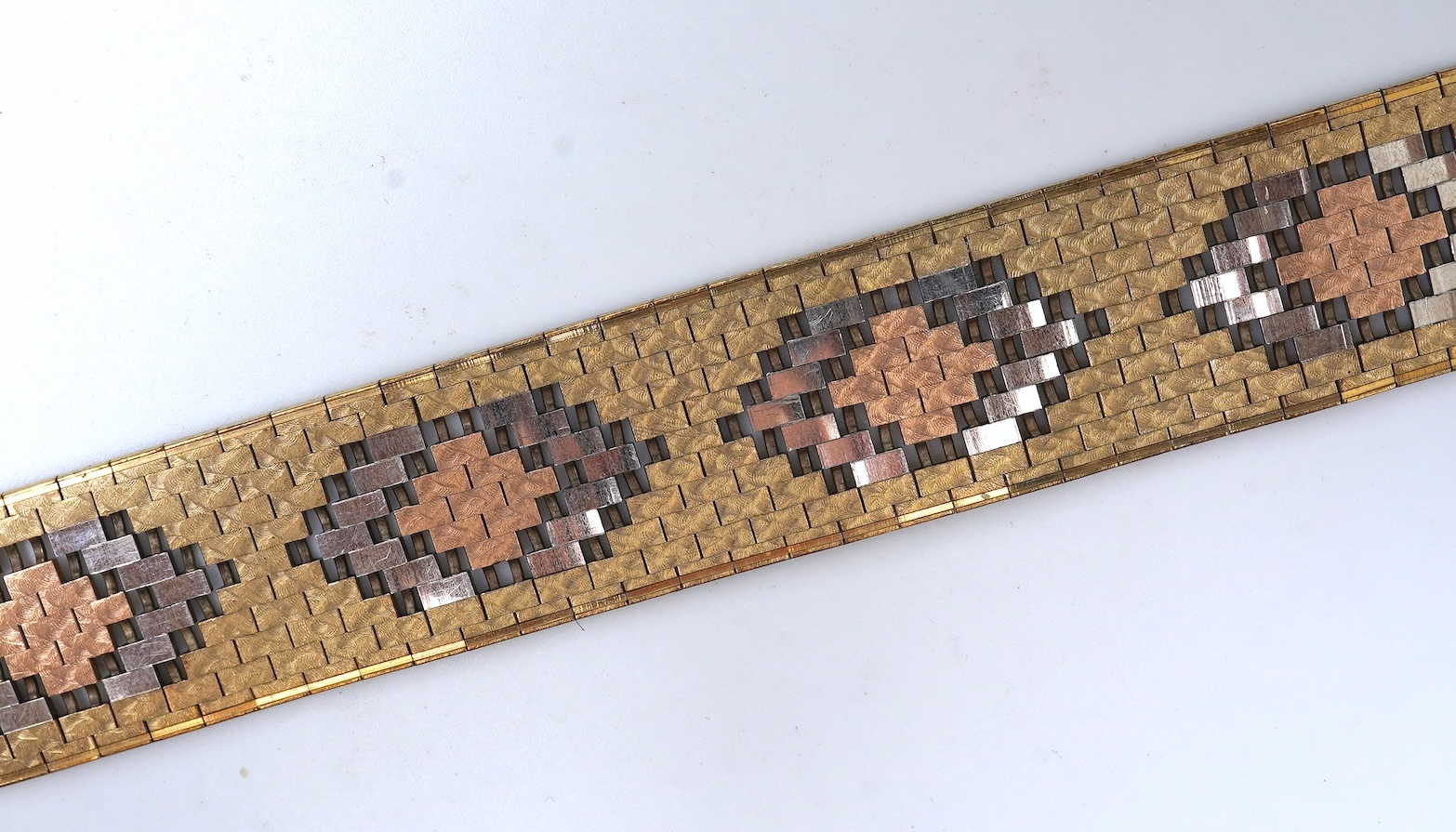 A gold bracelet, Italy, circa 1983, composed of brick linking with an engraved finish in tricoloured 9ct gold, length 18.5cm, Italian maker's mark, British import hallmarks, gross weight approximately 40.5 grams